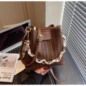 Close-up of woven bucket bag featuring floral scarf detail and golden chain handle