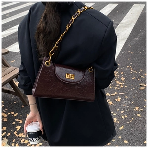 Detail of dark brown vintage textured leather shoulder bag with golden chain and twist lock