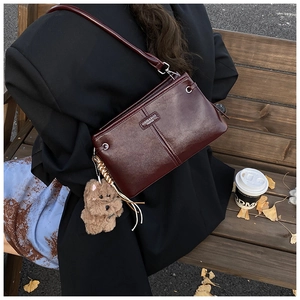 Sac à bandoulière vintage bordeaux avec charm d'ours en peluche dans un décor d'automne stylé