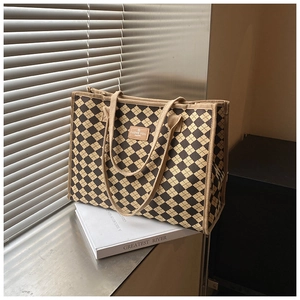 Detail of checkered canvas tote bag with a branded leather patch on a metallic surface