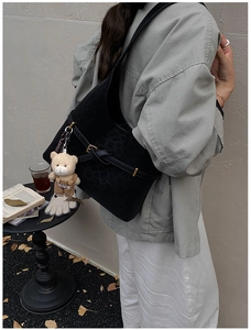 Detail of black leopard embossed shoulder bag featuring buckle strap and bear charm
