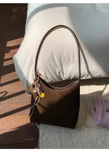Detail of dark brown suede tote bag with heart charm and tassel on white bedding