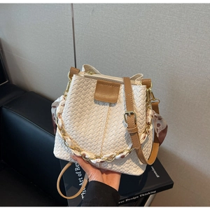 Detail of white woven bucket bag featuring gold chain and decorative floral scarf accent