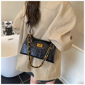 Close-up of black glossy crinkled leather shoulder bag with gold chain and turn-lock