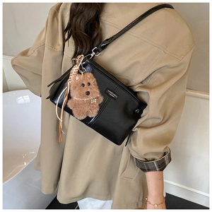 Détail du sac bandoulière en cuir noir brillant avec breloque chien peluche et étiquette