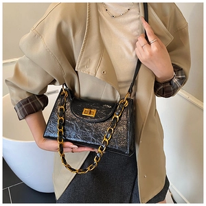 Detail of black crinkled patent leather shoulder bag with a gold chain and twist lock