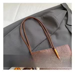 Dettaglio della borsa tote intrecciata marrone con manici in pelle e ciondolo in legno