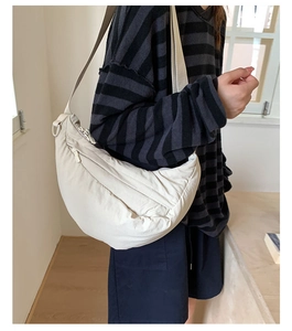 Detail of a beige crescent crossbody bag with soft quilted texture on striped outfit