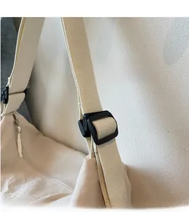 Detail of adjustable wide shoulder strap with durable black buckle on a beige tote bag