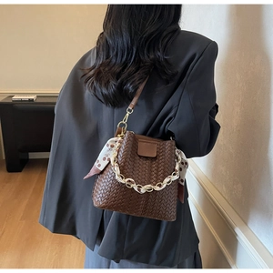 Detail of hand-woven brown leather bucket bag with silk scarf handle and chain strap