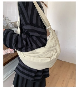 Beige crescent crossbody bag shown on person featuring soft nylon texture and adjustable strap