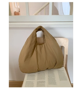 Detail of a puffer hobo bag in mustard yellow placed on a wooden chair with a magazine