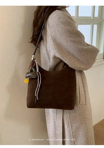Detail of dark brown suede tote bag with minimalist shoulder strap and stylish charms