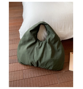 Detail of dark green pleated nylon tote bag with puffer texture on wooden floor