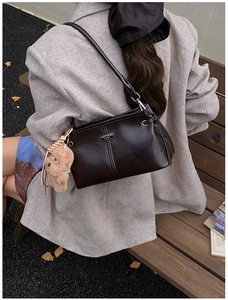 Détail du sac à bandoulière marron foncé brillant avec charm ours en peluche sur un banc