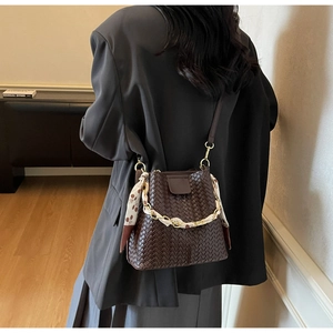Detail of a dark brown woven bucket bag featuring a gold chain and floral scarf accessory