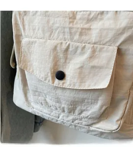 Detail of soft beige nylon fabric texture and front pocket with black snap button fastener