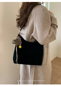 Detail view of black suede hobo bag featuring heart and smiley face charm accessories