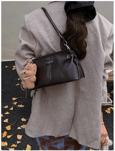 Détail d'un sac à main en cuir marron foncé avec breloque ours et logo de la marque
