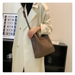 Brown leather tote bag worn with beige trench coat showing gold hardware and strap