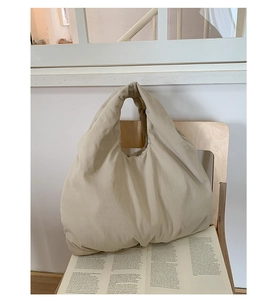 Close-up of beige pleated tote bag resting on a wooden chair with a magazine