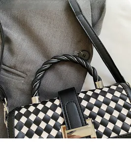 Detail of woven checkerboard handbag with twisted black handle and silver metal hardware