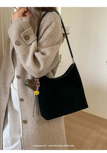 Detail of black suede tote bag with heart and smiley face charms on beige wool coat