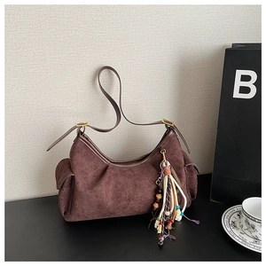 Detail of dark brown suede shoulder bag featuring ethnic tassel charm and gold hardware