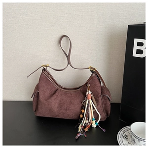 Detail of burgundy suede hobo bag featuring golden hardware and colorful tassel charm