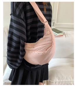 Side view of a pink crescent nylon crossbody bag worn by a model in a cozy home setting