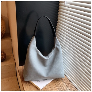 Détail du sac en tissu gris avec poignées en cuir noir texturé sur surface en bois