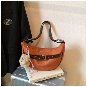 Detail of crescent shoulder bag in orange suede with brown leather strap and plush charm