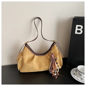 Detail of mustard suede hobo bag with side pockets and ethnic tassel keychain