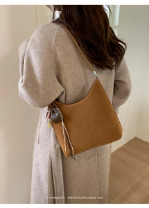Detail of a brown suede tote bag with a decorative heart charm and tassel accents