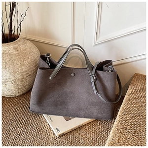 Close-up of dark grey suede tote bag with snap button closure on a textured mat