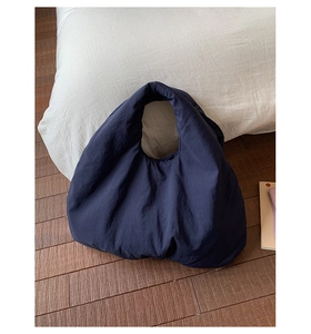 Detail view of navy blue puffer handbag with integrated handle on wooden floor