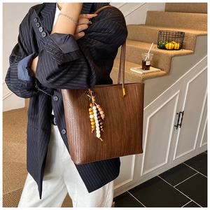 Dettaglio di una borsa tote marrone intrecciata con ciondolo in legno su modella in interni