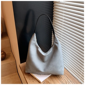 Détail du sac hobo gris clair avec poignée en cuir noir posé sur une surface en bois
