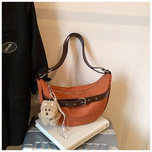 Detail of caramel suede crescent bag with dark leather strap and plush charm on luggage