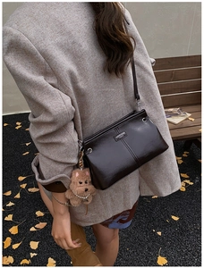 Détail du sac à bandoulière en cuir marron foncé avec breloque chien en peluche en automne