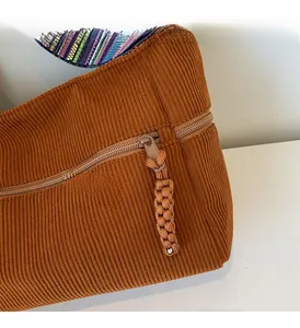 Detail of smooth zipper closure on brown corduroy tote bag with ethnic woven strap