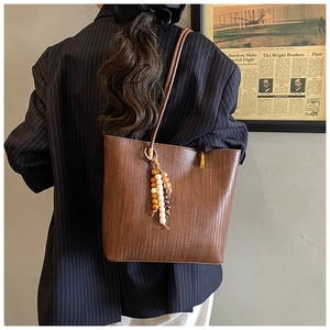 Dettaglio borsa tote marrone intrecciata con nappa di perline su blazer blu