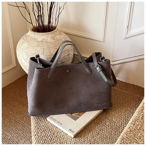 Detail of grey suede tote bag with magnetic clasp and adjustable strap in lifestyle setting