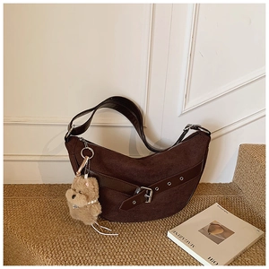 Detail view of dark brown crescent shoulder bag with suede texture and plush puppy charm