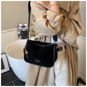 Detail der schwarzen Wildleder-Tasche mit Fashion-Logo und dekorativen Holzperlen