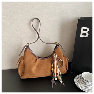 Detail of suede hobo bag featuring brown leather trim and ethnic beaded tassel charm