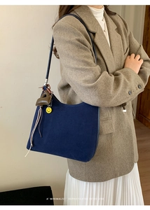 Detail view of navy blue suede hobo bag with a yellow smiley face charm on a model