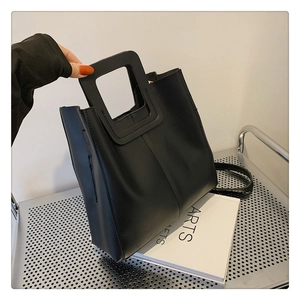 Close-up of minimalist black leather tote bag featuring a unique hollow handle and stitching