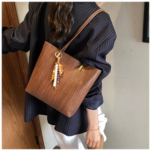 Dettaglio borsa tote marrone intrecciata con nappa di perline colorate e fibbia in metallo