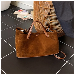 Close-up of brown suede tote bag with leather straps on a dark tiled floor